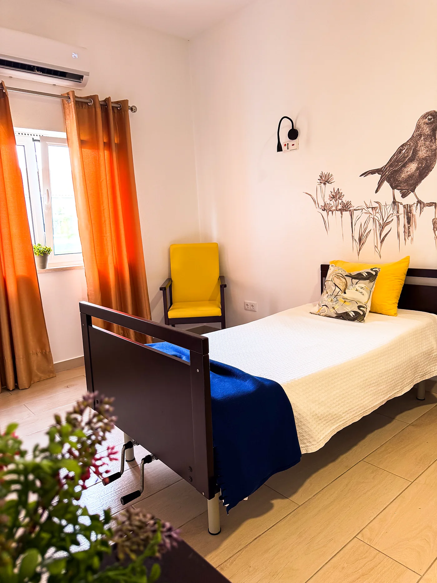 Quarto individual com cadeirão amarelo junto à janela